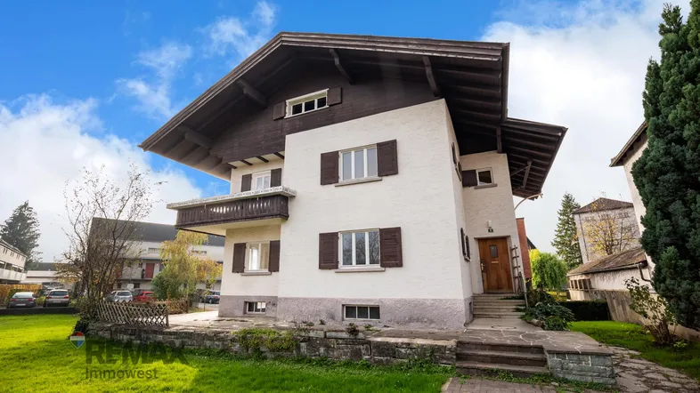 Traditionelles Haus mit weißer Fassade, braunen Fensterläden und einem gepflegten Vorgarten.