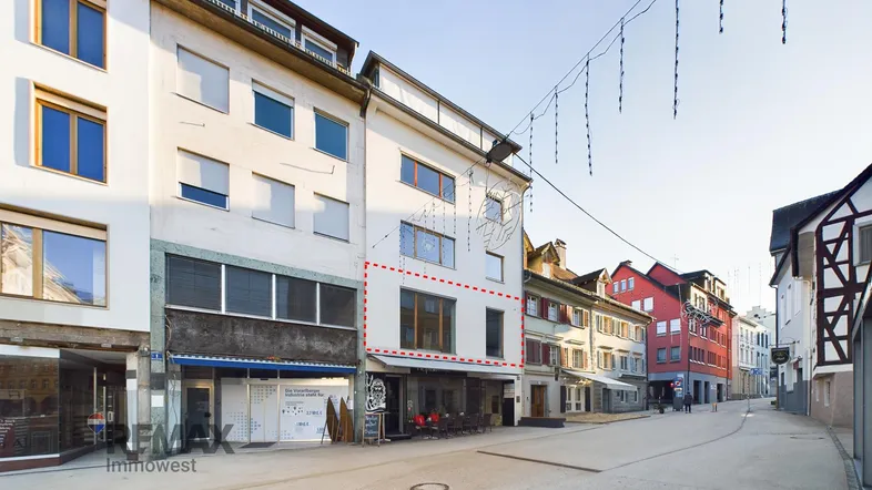 Ansicht der Gebäudefassade an einer belebten Straße mit Geschäften im Erdgeschoss und Wohnungen darüber.