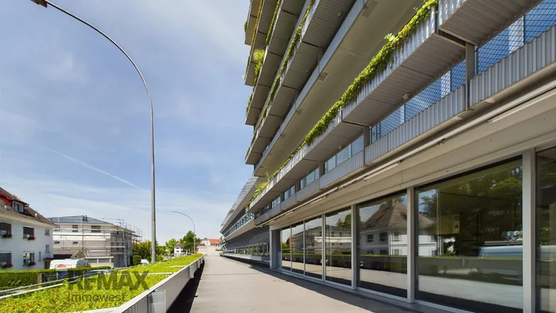 Moderne Architektur mit mehreren Etagen, Balkonen und begrünten Fassadenbereichen entlang eines Gehwegs.