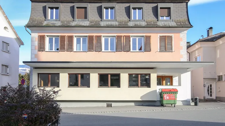 Klassisches Gebäude mit Mansarddach, hellrosa Fassade und braunen Fensterläden.