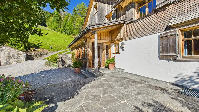 Eingangsbereich eines traditionellen Holzhauses mit Steinfliesen und Blick auf die grüne Hügellandschaft.