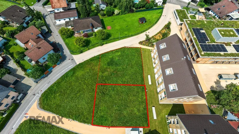 Luftaufnahme eines Baugrundstücks mit roter Markierung und umliegenden Gebäuden in grüner Umgebung.