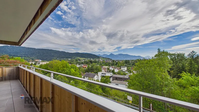 Geräumiger Balkon mit Holzelementen und weitem Blick über das Tal und die umliegenden Berge.