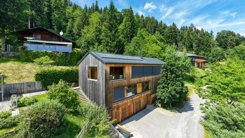 Modernes Holzhaus in Hanglage, umgeben von grünen Wäldern und Natur.