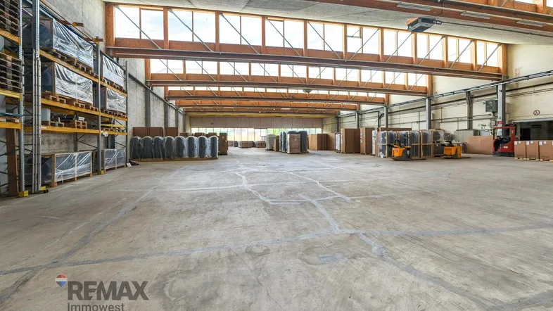 Geräumige Lagerhalle mit hohen Decken, Holzbalken und großen Fenstern, die viel Tageslicht hereinlassen.