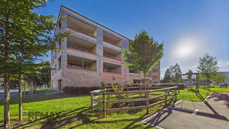 Modernes Mehrfamilienhaus mit Holzfassade und mehreren Balkonen unter strahlendem Sonnenschein.