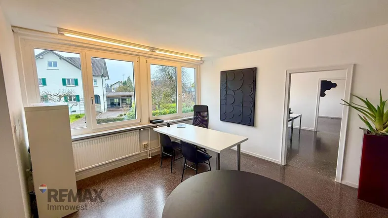 Helles Büro mit großen Fenstern, Blick ins Grüne und modernem Mobiliar für einen Arbeitsplatz.