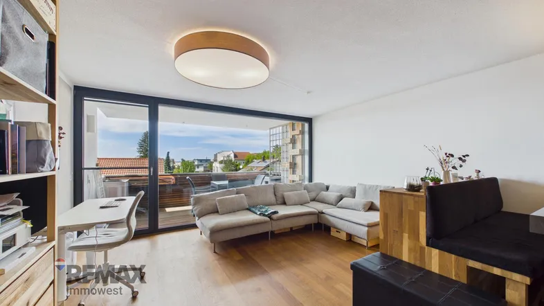 Helles Wohnzimmer mit Holzboden, großem Sofa und Zugang zu einem Balkon mit Aussicht.