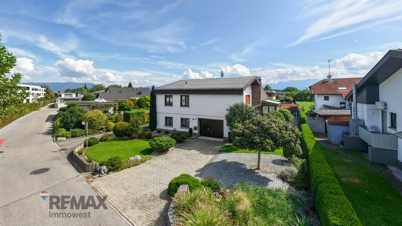 Einfamilienhaus mit gepflegtem Vorgarten, großer Auffahrt und Blick auf die umliegende Landschaft.