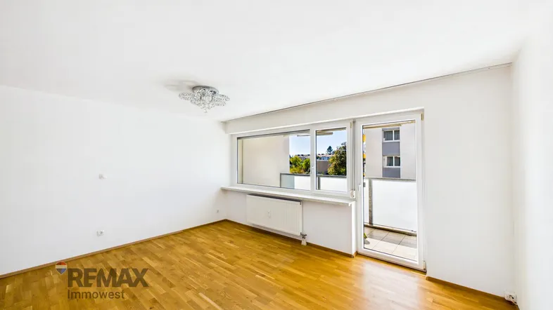 Helles Wohnzimmer mit Parkettboden, weiß gestrichenen Wänden und Zugang zum Balkon.