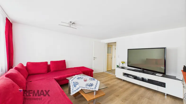 Helles Wohnzimmer mit rotem Ecksofa, Holzboden und einem modernen TV-Möbel.