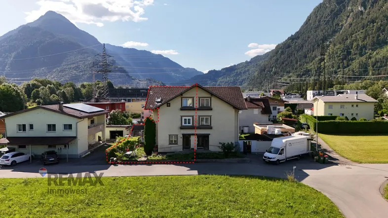 Ländliches Einfamilienhaus mit Bergblick und umgebender Natur unter blauem Himmel.