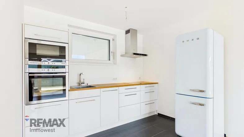 Moderne Küche mit weißen Schränken, Holzarbeitsplatte, integrierten Geräten und einem freistehenden Retro-Kühlschrank.