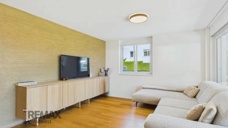 Helles Wohnzimmer mit Holzboden, modernem Sofa und einer strukturierten Akzentwand.