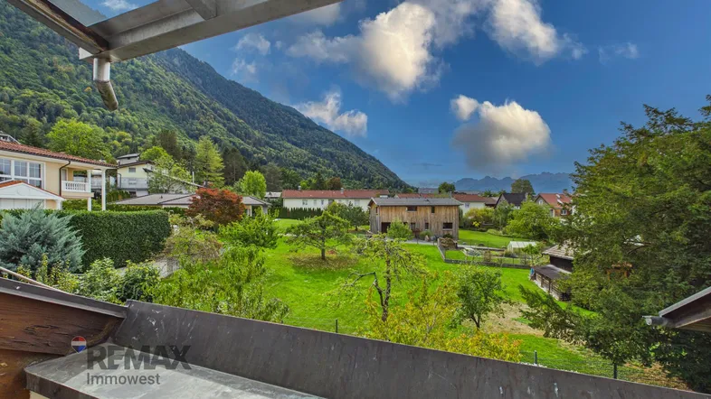 Weitläufiger Blick auf die grüne Berglandschaft und umliegende Häuser unter blauem Himmel.