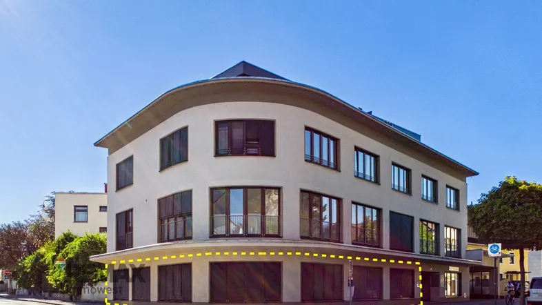 Modernes Geschäftsgebäude an einer Straßenecke mit großen Fenstern und einer markanten runden Architektur.