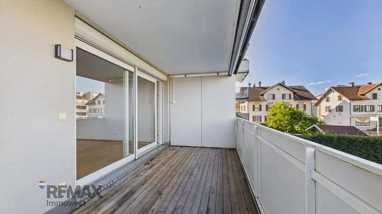Helles Balkon mit Holzboden und Blick auf die umliegenden Häuser und Grünflächen.