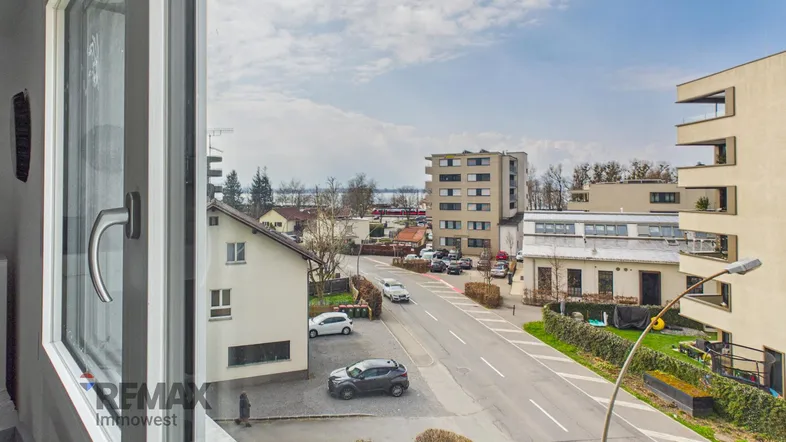 Blick aus dem Fenster auf die Straße, umliegende Gebäude und einen See in der Ferne.