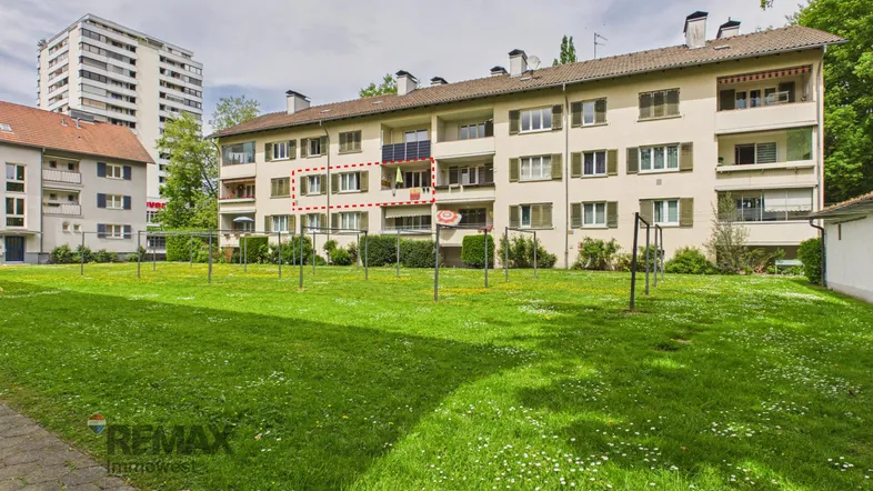 Mehrfamilienhaus mit großem Gemeinschaftsgarten und Balkonen in einer grünen Umgebung.