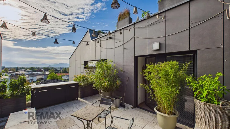 Geräumige Dachterrasse mit Essbereich, Pflanzen und Blick auf die Umgebung unter blauem Himmel.