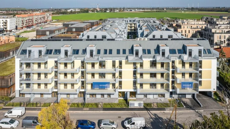 Modernes Mehrfamilienhaus mit vielen Balkonen und Blick auf die umliegende Landschaft.