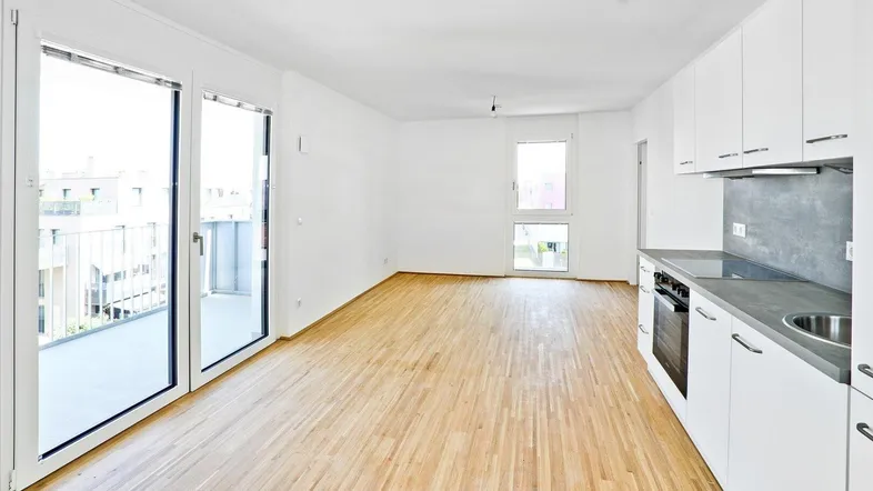 Heller Wohn- und Essbereich mit integrierter Küchenzeile, Parkettboden und Zugang zum Balkon.