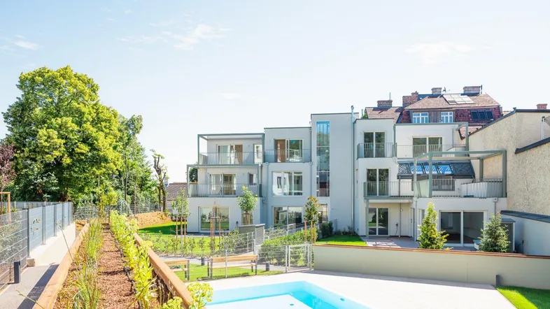 Modernes Wohngebäude mit Balkonen, umgeben von Grünflächen und einem privaten Poolbereich.