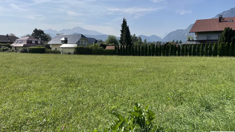Sonnige Grünfläche mit angrenzenden Häusern und Panoramablick auf die Berglandschaft.