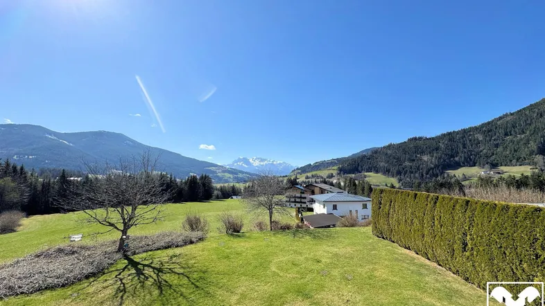 Weitläufiger Blick über grüne Wiesen und Berge unter strahlend blauem Himmel.