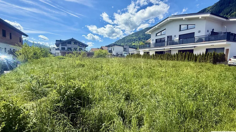 Großes unbebautes Grundstück mit Blick auf moderne Häuser und die umliegende Berglandschaft.