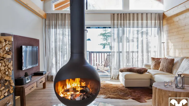 Gemütliches Wohnzimmer mit modernem Hängekamin, Holzboden und Blick auf den See.