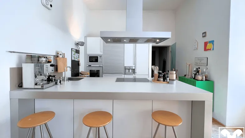 Moderne Küche mit weißer Arbeitsplatte, integriertem Kochfeld und Barhockern für eine gemütliche Atmosphäre.