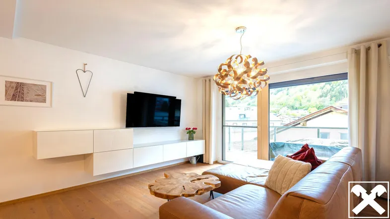 Helles Wohnzimmer mit modernem Design, bequemer Ledercouch und Zugang zum Balkon mit Bergblick.
