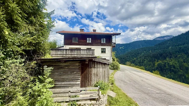 Haus in den Bergen mit Holzanbau und weitem Blick auf die bewaldete Landschaft.