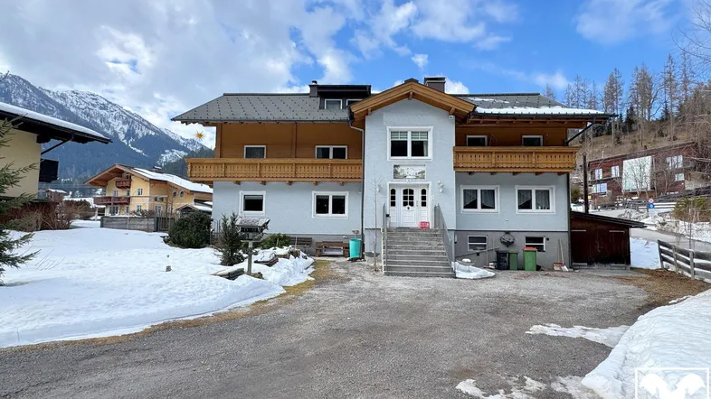 Großes Wohnhaus in alpiner Umgebung mit Balkonen und verschneiter Landschaft im Winter.