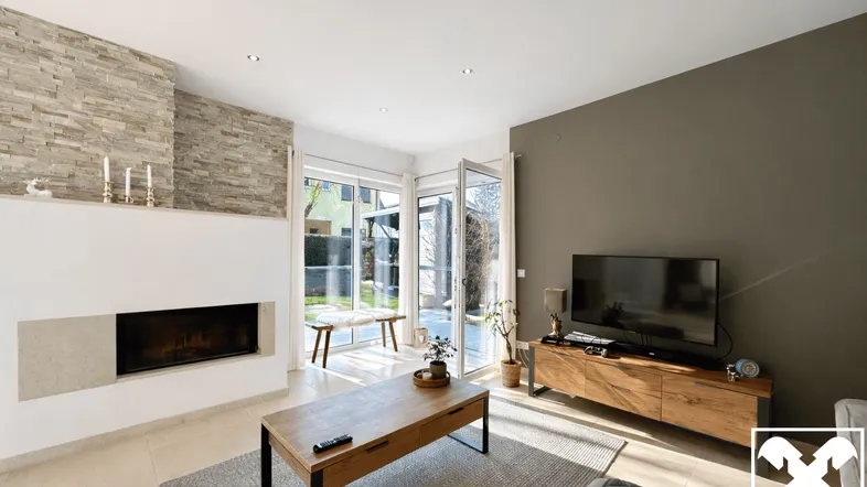 Helles Wohnzimmer mit modernem Kamin, Steinwand und Zugang zum Gartenbereich.