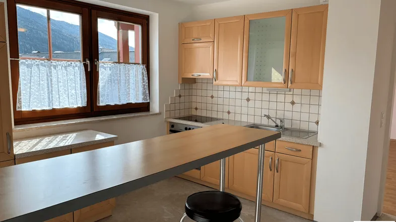 Helle Küche mit Holzschränken, Fliesenspiegel und integrierter Frühstücksbar mit Bergblick.