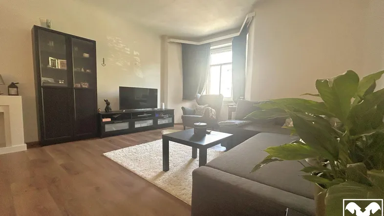 Helles Wohnzimmer mit Holzboden, gemütlichem Sofa und Fernseher, ideal für entspannte Abende.