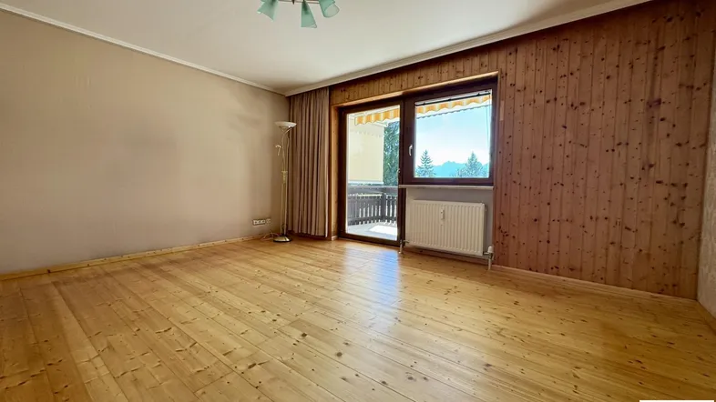 Helles Wohnzimmer mit Holzplankenboden, Holzwandverkleidung und Zugang zu einem Balkon mit Bergblick.