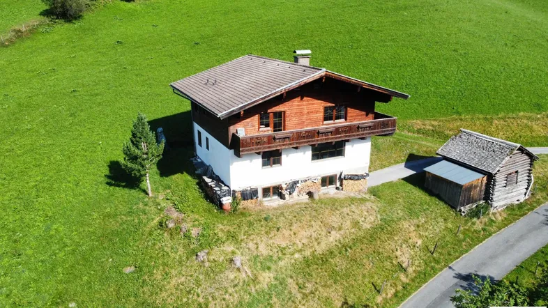 Traditionelles Haus im Chalet-Stil mit Satteldach und Holzbalkonen, umgeben von grünen Wiesen.