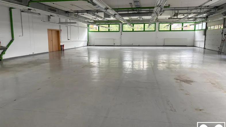 Geräumige, leere Produktionshalle mit Betonboden, hohen Decken und großen Fenstern für viel Tageslicht.