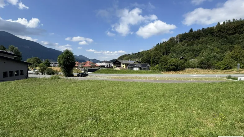 Weitläufige Grünfläche mit Blick auf die umliegende Berglandschaft und einige Gebäude in der Ferne.