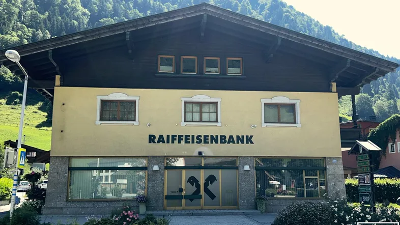 Gebäude der Raiffeisenbank mit traditioneller Architektur und Bergblick im Hintergrund.