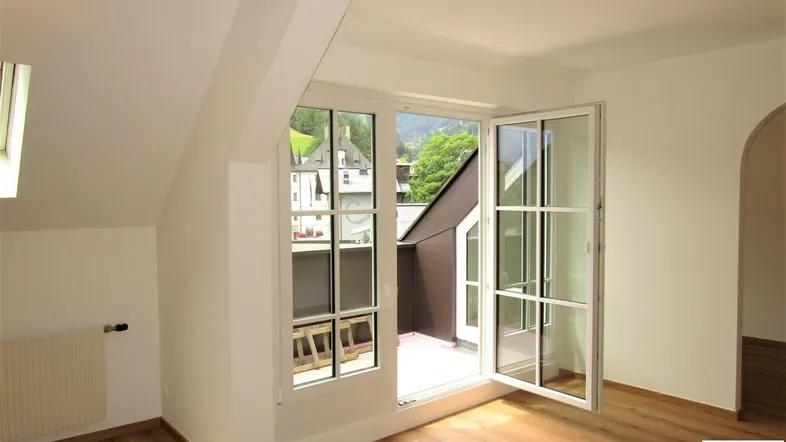 Heller Wohnraum mit Holzboden, Dachschräge und Zugang zu einem kleinen Balkon mit Bergblick.