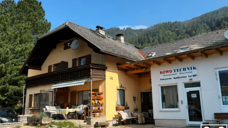 Traditionelles Gebäude mit angrenzendem Geschäft und Sitzbereich im Freien, umgeben von Bergen.