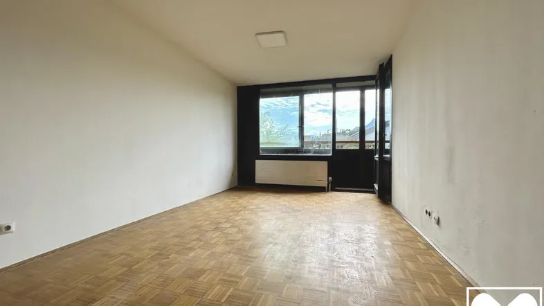 Heller Raum mit Fischgrätparkettboden und großen Fenstern, die viel Tageslicht hereinlassen.