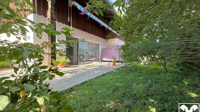 Sonnige Terrasse mit Zugang zum Garten, umgeben von üppigem Grün und Pflanzen.