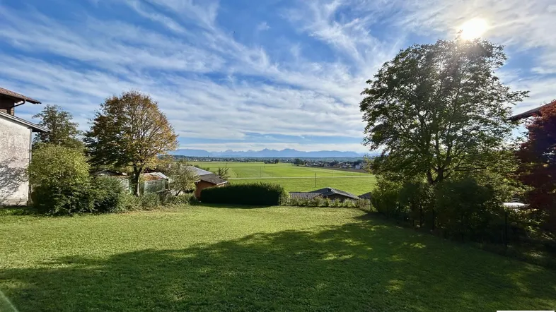Weitläufige Rasenfläche mit altem Baumbestand und Panoramablick auf die umliegende Landschaft und Berge.