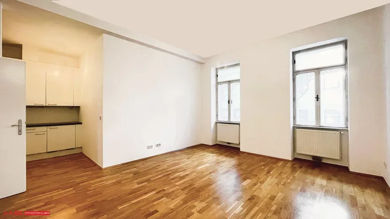 Heller Wohnbereich mit Parkettboden und integrierter Küchenzeile, ideal für offenes Wohnen.