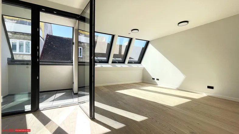 Helles Wohnzimmer im Dachgeschoss mit Holzboden, Dachfenstern und Zugang zu einem kleinen Balkon.